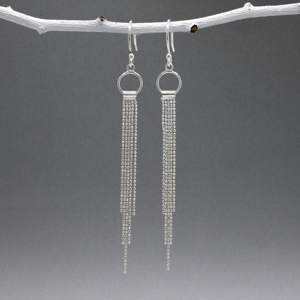 Áine Chains on Ring Silver Dangle Earrings. These handmade sterling silver earrings feature a delicate ring adorned with cascading chains, offering a unique and elegant look. Features: Material: Handmade sterling silver Design: Chains on a 9mm diameter ring Chain Width: 4mm at the widest area Length: 87mm from the top of the French wire hook Finish: Highly polished Closure: French wire hook for a secure and comfortable fit