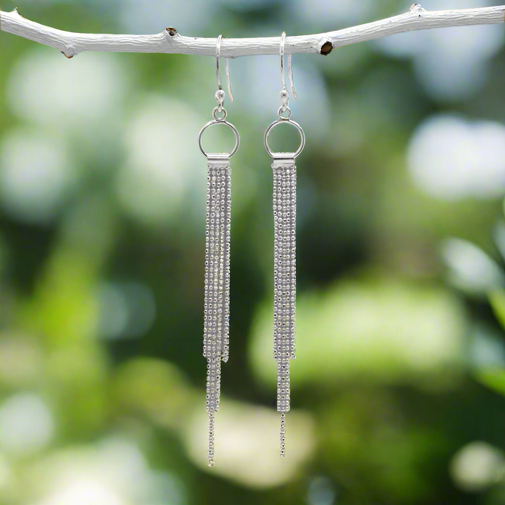 Handcrafted in solid .925 sterling silver, the Áine Cascading Chains on Small Hoop Silver Dangle Earrings offer a fresh twist on a classic hoop. Cascading chains flow gently from each polished hoop, creating natural movement and shine as you wear them.
These lightweight earrings are designed for comfortable all-day wear, with a modern finish that suits both casual looks and special occasions. The secure sterling silver French wire hooks include clear rubber stoppers for added peace of mind.
