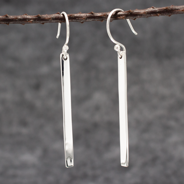 Artemis Slab Earrings: handcrafted elegance! Picture sterling silver gracefully dangling, adding timeless beauty to any look. These sleek earrings measure 40mm long by 3mm wide (approx. 1 & 5/8 inches long by 1/8 inches wide). Crafted from .950 sterling silver with a high-polished finish, they're wearable art. With secure dangle French wires, they offer comfort all day. 