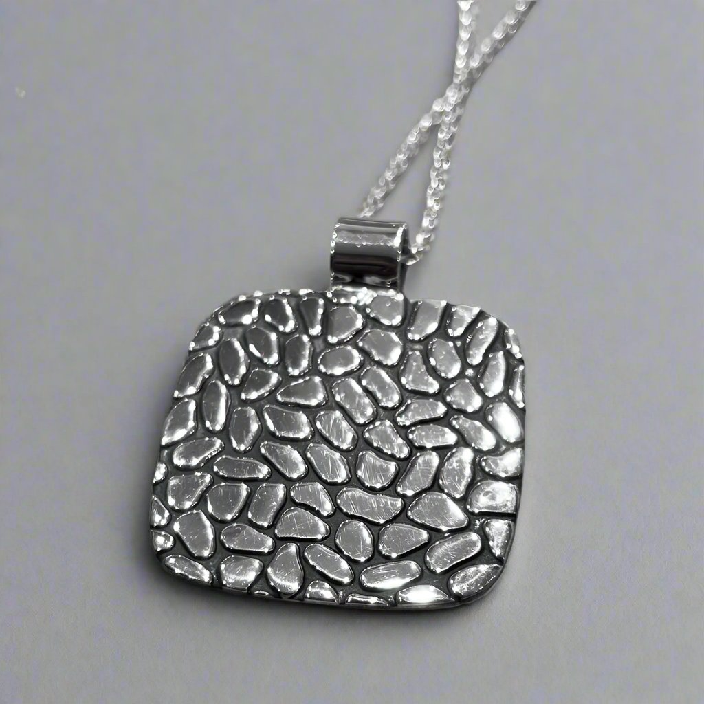 The Camila Square Oxidised Silver Pendant features a bold square design with a striking cobblestone pattern, blending oxidized and highly polished finishes. Crafted from .950 sterling silver, this pendant offers a unique texture that catches the eye.
Material: .950 sterling silver with oxidized and highly polished finishes, featuring a cobblestone pattern
Dimensions:
Size: 30mm long by 30mm wide (1 1/8 inches long by 1 1/8 inches wide)
Chain: Includes a 2.5mm sterling silver Rolo chain with a lobster claw