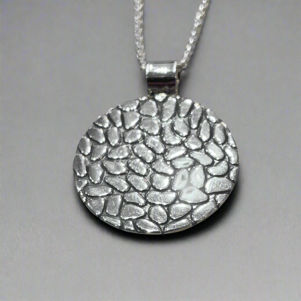 The Camila Disc Oxidised Silver Pendant features a bold, circular design with a striking cobblestone pattern. Crafted from .950 sterling silver, this pendant blends an oxidized texture with a highly polished silver finish.
Material: .950 sterling silver with an oxidized cobblestone pattern and highly polished finish
Dimensions:
Diameter: 30mm (1 3/16 inches)
Chain: Includes a 2.5mm sterling silver Rolo chain with a lobster claw clasp (select your preferred length)
Bail: Tube bail fits up to a 5mm chain (3/
