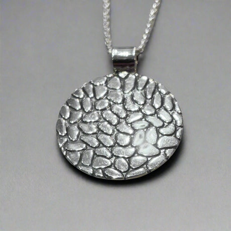 The Camila Disc Oxidised Silver Pendant features a bold, circular design with a striking cobblestone pattern. Crafted from .950 sterling silver, this pendant blends an oxidized texture with a highly polished silver finish.
Material: .950 sterling silver with an oxidized cobblestone pattern and highly polished finish
Dimensions:
Diameter: 30mm (1 3/16 inches)
Chain: Includes a 2.5mm sterling silver Rolo chain with a lobster claw clasp (select your preferred length)
Bail: Tube bail fits up to a 5mm chain (3/