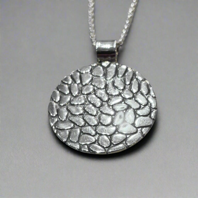 The Camila Disc Oxidised Silver Pendant features a bold, circular design with a striking cobblestone pattern. Crafted from .950 sterling silver, this pendant blends an oxidized texture with a highly polished silver finish.
Material: .950 sterling silver with an oxidized cobblestone pattern and highly polished finish
Dimensions:
Diameter: 30mm (1 3/16 inches)
Chain: Includes a 2.5mm sterling silver Rolo chain with a lobster claw clasp (select your preferred length)
Bail: Tube bail fits up to a 5mm chain (3/