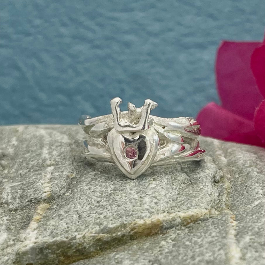Double Claddagh Silver Ring with a Touch of Pink Tourmaline Design: Organic Claddagh inspired by twigs and Irish coral Material: Solid sterling silver cast Finish: Highly polished Band: 7.5mm in width Centre: Heart and crown measure 13mm long Accent: 1mm pink tourmaline A beautifully crafted piece that blends tradition with nature’s elegance. Perfect for expressing love, loyalty, and friendship.