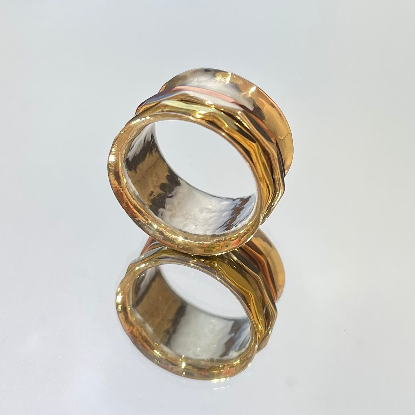 The Tara Mixed Metal Spinning Silver Ring is a true statement piece, boasting a 13mm-wide band for a bold yet comfortable fit. Its intricate design features three inner bands crafted from brass, copper, and silver, each measuring 2mm wide. This ring is a stunning fusion of style and craftsmanship, sure to turn heads wherever you go.