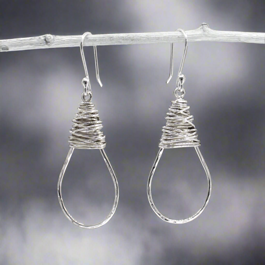 The Saha Drop Shape with Wire Wrap Silver Earrings bring timeless elegance to your jewellery collection. Handcrafted from sterling silver, these earrings feature a graceful drop shape accentuated with intricate wire wrapping. The highly polished finish adds a refined touch, making them ideal for both everyday wear and special occasions. Ireland jewellery