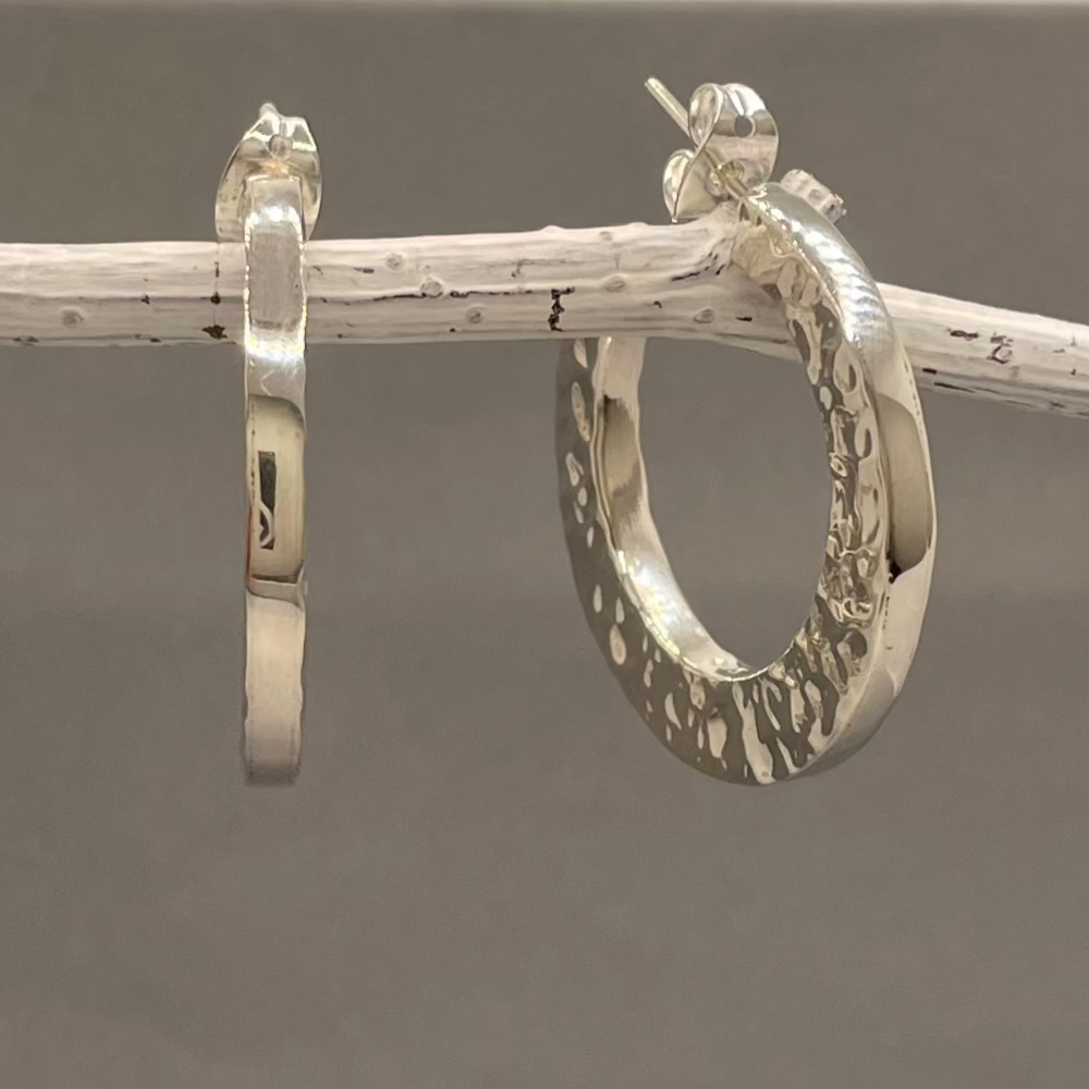 The Saha Geometric Hammered Hoop Silver Earrings exude understated elegance with their minimalist and modern design. These handcrafted sterling silver hoops feature a beautifully hammered texture on both sides, complemented by a polished gloss finish on the front. Perfect for cocktail parties or daily wear, they offer a timeless charm to suit any occasion. ireland gifts jewellery