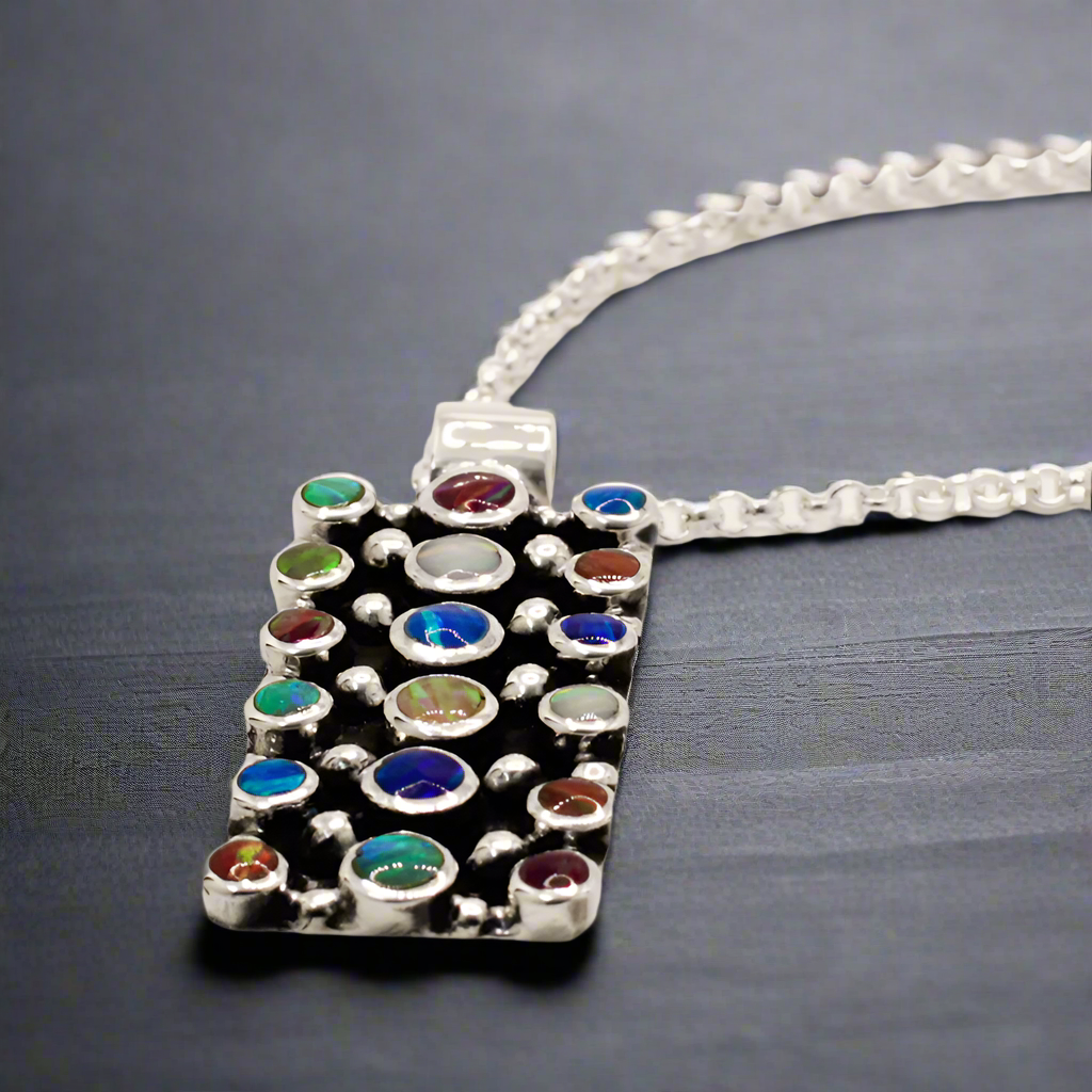 Sleveen Rectangle with Round Multi-Coloured Opalescence Mosaic Resin Silver Pendant. Sleveen's Rectangle with Round Multi-Coloured Opalescence Mosaic Resin Silver Pendant is a bold, statement piece that captures the vibrant charm of Kinsale. Featuring a blend of multi-coloured opalescent resin, this pendant reflects the lively, confetti-like hues of Kinsale’s iconic houses, adding a unique splash of colour to your collection.