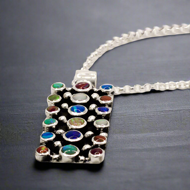 Sleveen Rectangle with Round Multi-Coloured Opalescence Mosaic Resin Silver Pendant. Sleveen's Rectangle with Round Multi-Coloured Opalescence Mosaic Resin Silver Pendant is a bold, statement piece that captures the vibrant charm of Kinsale. Featuring a blend of multi-coloured opalescent resin, this pendant reflects the lively, confetti-like hues of Kinsale’s iconic houses, adding a unique splash of colour to your collection.