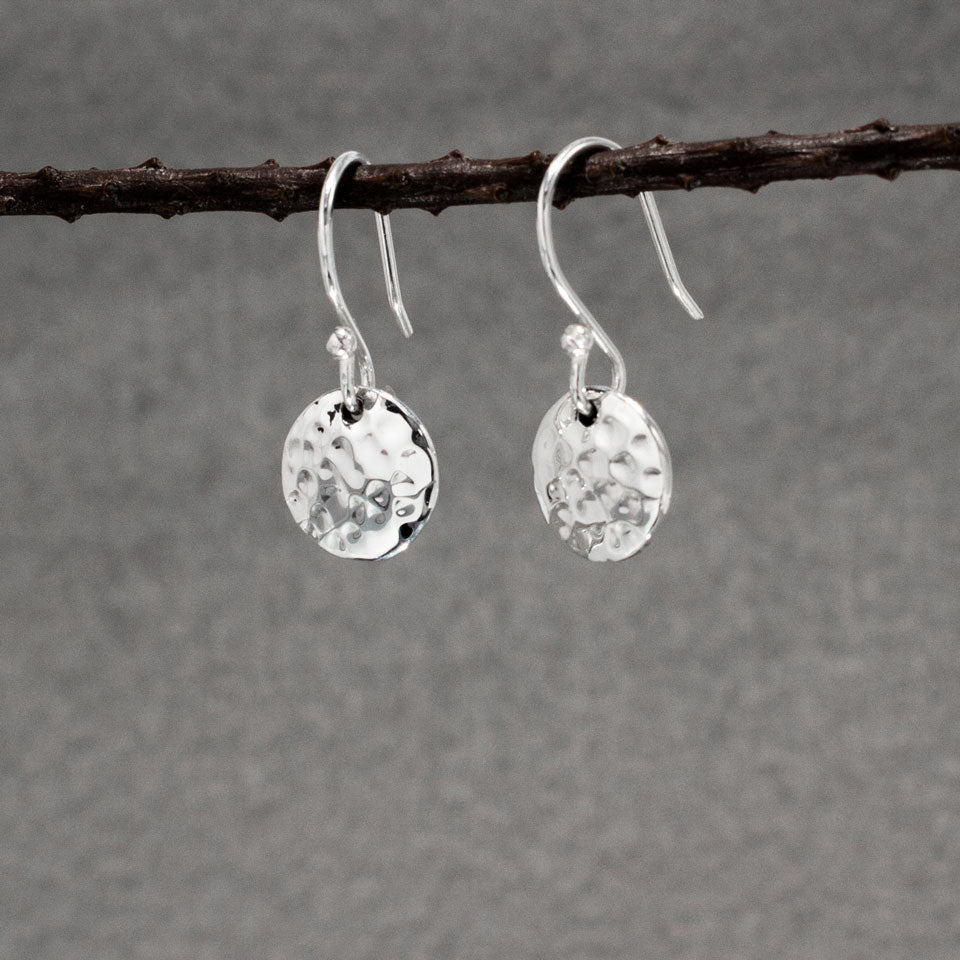 These Artemis earrings are crafted from .950 sterling silver and feature a beautiful hammered finish, adding unique texture. Material: .950 sterling silver Dimensions: Disc Diameter: 10 mm (approx. 3/8 inches) Total Length (from top of ear wire): 22 mm (approx. 7/8 inches) Design: Dangle earrings with a hammered finish Closure: Sterling silver French wire These earrings are perfect for any outfit.