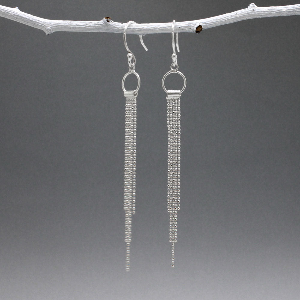 Áine Chains on Ring Silver Dangle Earrings. These handmade sterling silver earrings feature a delicate ring adorned with cascading chains, offering a unique and elegant look.  Features:  Material: Handmade sterling silver Design: Chains on a 9mm diameter ring Chain Width: 4mm at the widest area Length: 87mm from the top of the French wire hook Finish: Highly polished Closure: French wire hook for a secure and comfortable fit