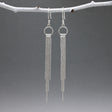 Áine Chains on Ring Silver Dangle Earrings. These handmade sterling silver earrings feature a delicate ring adorned with cascading chains, offering a unique and elegant look.  Features:  Material: Handmade sterling silver Design: Chains on a 9mm diameter ring Chain Width: 4mm at the widest area Length: 87mm from the top of the French wire hook Finish: Highly polished Closure: French wire hook for a secure and comfortable fit