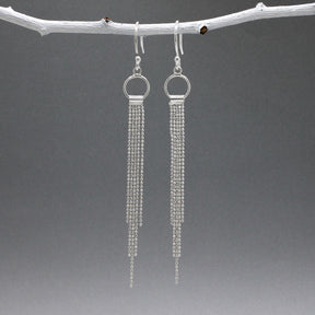 Áine Chains on Ring Silver Dangle Earrings. These handmade sterling silver earrings feature a delicate ring adorned with cascading chains, offering a unique and elegant look. Features: Material: Handmade sterling silver Design: Chains on a 9mm diameter ring Chain Width: 4mm at the widest area Length: 87mm from the top of the French wire hook Finish: Highly polished Closure: French wire hook for a secure and comfortable fit