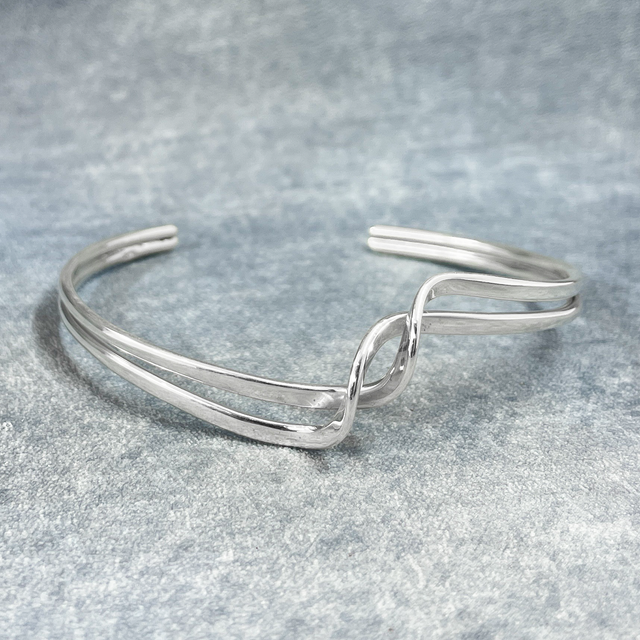 Uisce - Soft Double Wave with Crest Cuff Silver Bracelet, meticulously crafted from sterling silver and polished to perfection. This bracelet offers a thickness of 2 millimetres and can be effortlessly adjusted to ensure a perfect fit. Measuring 15 cm on the inner length and 16 cm on the outer length, with a width of 2 cm at its widest point and a 3 cm gap.