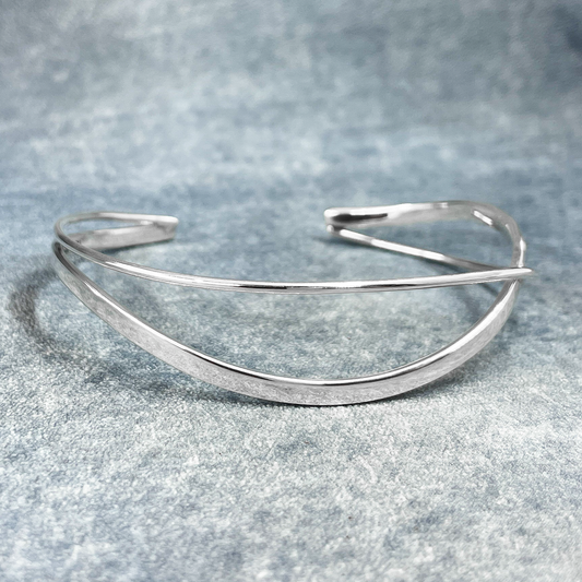 Uisce - Double Wave Cuff Silver Bracelet, meticulously handcrafted with sterling silver and boasting a striking high-polished finish. Each cuff features a captivating Double Wave design, accentuated by polished silver. This handmade piece offers a thickness of 1.5 millimeters and can be gently adjusted for a perfect fit.</p> <p>Measuring 14.5 cm on the inner length and 15.5 cm on the outer length from end to end, with a width of 1.2 cm at its widest point and a 3 cm gap.