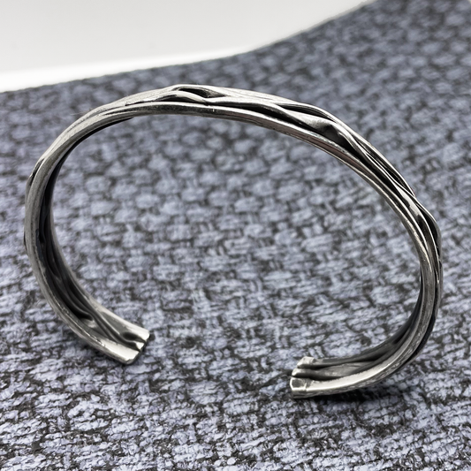 Uisce - Corrugated Oxidised Narrow Cuff Silver Bracelet, a testament to exquisite craftsmanship and timeless elegance. With a thickness of 4 millimetres, while its adjustable design allows for a customized fit that's just right for you. Measuring 15.6 cm on the inner length and 18 cm on the outer length, with a width of 8 millimeters and a 2.8 cm gap, this versatile bracelet is perfect for any occasion, from casual outings to special events.