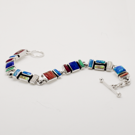 Add a vibrant pop of colour to your style with the Sleveen bracelet. Seven colorful rectangle opalescent pieces display a mesmerizing mosaic, measuring 7mm in width and 3mm deep. This bracelet is finished with a toggle clasp and measures 19cm in length, crafted in .925 silver and featuring colored resins inspired by the beautiful houses of Kinsale.