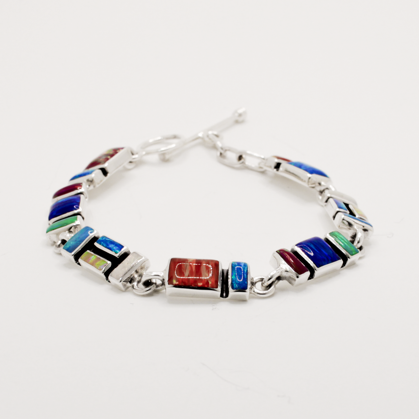 Add a vibrant pop of colour to your style with the Sleveen bracelet. Seven colorful rectangle opalescent pieces display a mesmerizing mosaic, measuring 7mm in width and 3mm deep. This bracelet is finished with a toggle clasp and measures 19cm in length, crafted in .925 silver and featuring colored resins inspired by the beautiful houses of Kinsale.