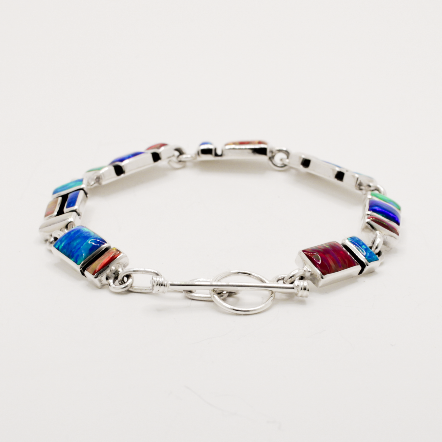 Add a vibrant pop of colour to your style with the Sleveen bracelet. Seven colorful rectangle opalescent pieces display a mesmerizing mosaic, measuring 7mm in width and 3mm deep. This bracelet is finished with a toggle clasp and measures 19cm in length, crafted in .925 silver and featuring colored resins inspired by the beautiful houses of Kinsale.