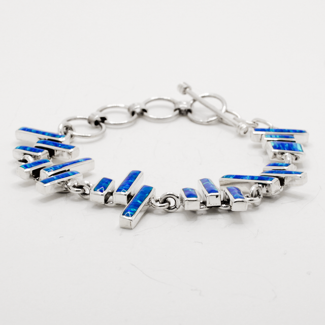 Sleveen's Blue Resin Opalescent Kinsale Steps Bracelet is a real showstopper! Crafted with a grand 18mm width, 3mm depth, and 19cm length, this bracelet features eye-catching blue opalescent resin steps. The toggle clasp is adjustable from 6" to 7.5" and made of .925 silver, making it a uniquely beautiful piece. Immerse yourself in the beauty of the stellar wild Atlantic with the mesmerizing blue hues of this bracelet!