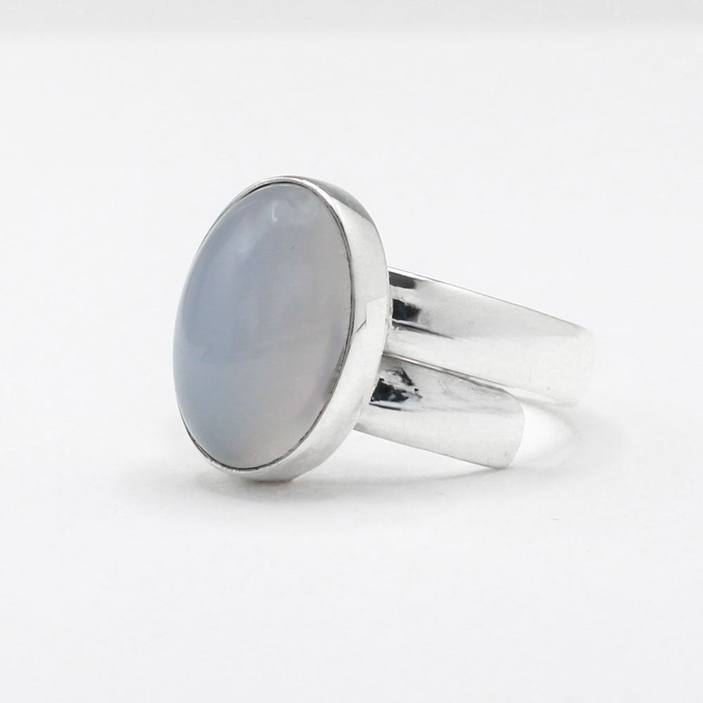 This exquisite ring features an oval blue chalcedony stone with a delicate light pink hue, set in high-quality sterling silver. The cabochon cut highlights the gemstone's natural beauty, while the adjustable band ensures a perfect fit for any wearer. This elegant piece adds a touch of sophistication and color to any outfit.