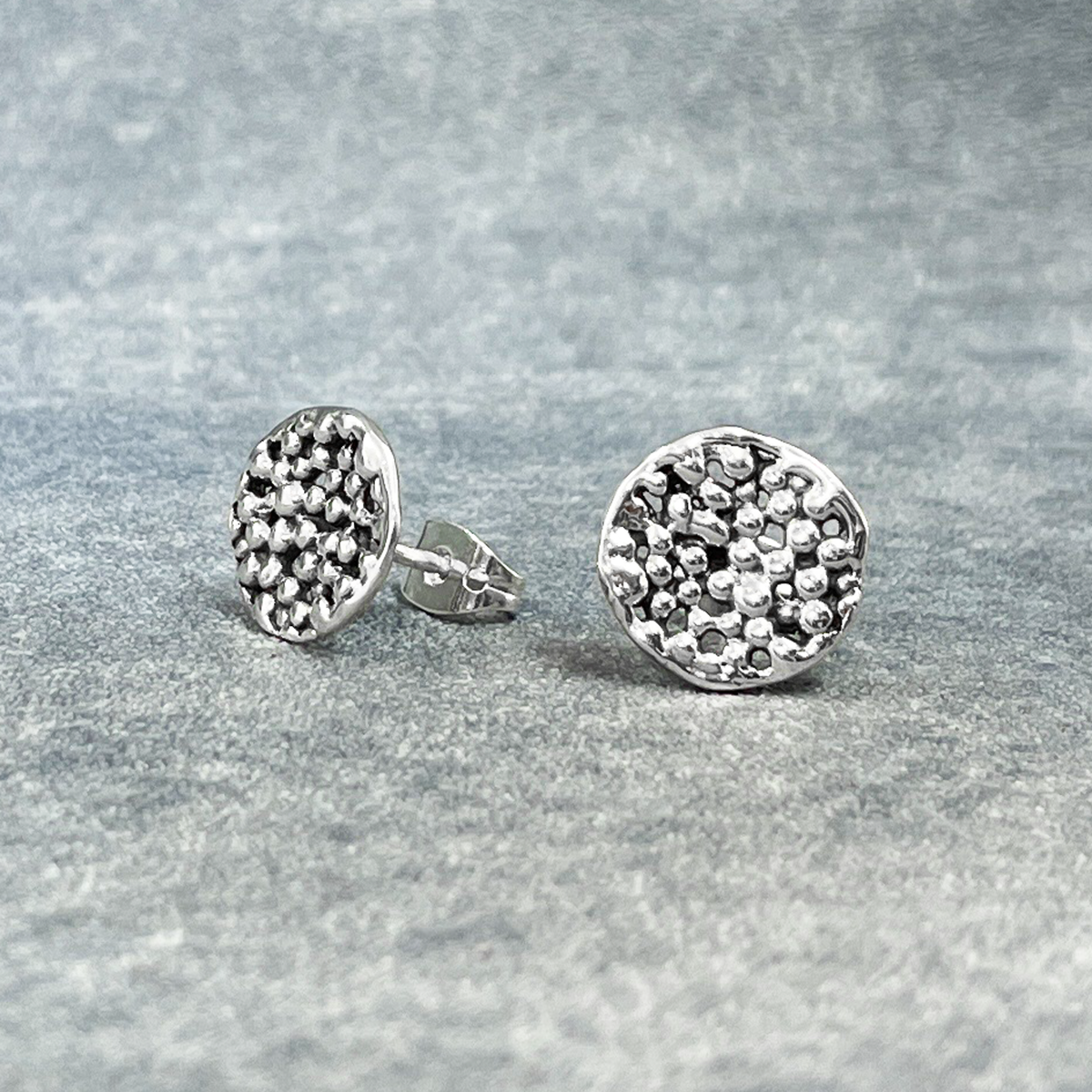 Uisce - Sea Foam Silver Earrings - Stud, meticulously handcrafted with sterling silver and boasting a high-polished finish. These earrings feature a unique texture resembling sea foam.  Expertly handmade with a thickness of 2 millimeters, they also feature sterling silver friction posts. Measuring 12 millimeters in diameter.