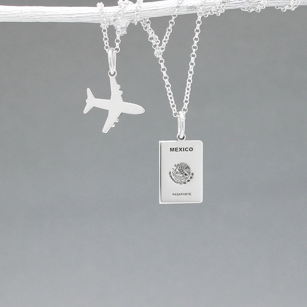 Our Mexican Passport Mini Replica Silver Pendant captures the intricate details of a Mexican passport cover, meticulously crafted from sterling silver with a high-polished finish.  Dimensions: Passport: 10mm wide by 14mm high; Airplane: 14mm wide by 14mm high. Bail: Fits up to a 2.5mm chain for versatile wear. Chain: Includes a 1.4mm sterling silver belcher Rolo chain, available in various lengths.