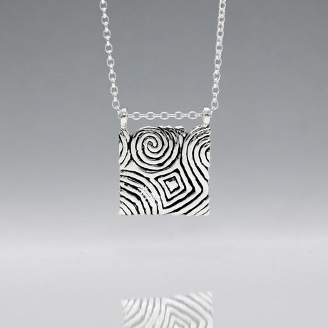 Inspired by the Newgrange Stone  Dimensions: 20mm wide x 24mm high (including bail), 2mm thick Finish: Oxidized to accentuate the design, with a high polished finish Material: Handmade with 0.50 sterling silver Chain: 1.7mm sterling silver rolo chain included (select chain size below) Celebrate the ancient beauty of Newgrange with our Cropped Square Silver Pendant. This unique piece is expertly crafted to honor Ireland's rich heritage.