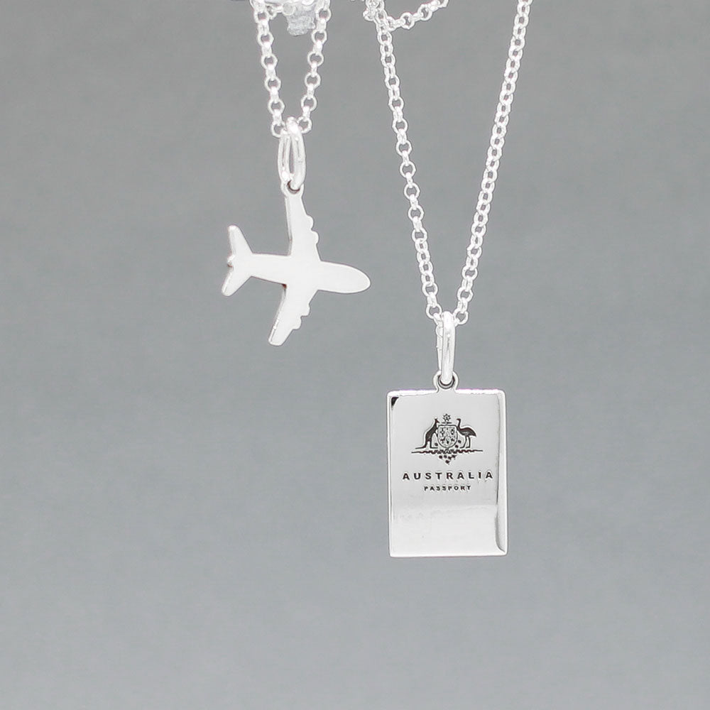 Our Australian Passport Mini Replica Silver Pendant captures all the intricate details of a passport cover. Meticulously crafted from sterling silver, it boasts a dazzling high-polished finish.  Dimensions: Passport: 10mm wide by 14mm high Airplane: 14mm wide by 14mm high Bail: Fits up to a 2.5mm chain for versatile wear. Chain: Includes a 1.4mm sterling silver belcher Rolo chain, available in various lengths to suit your style preference.