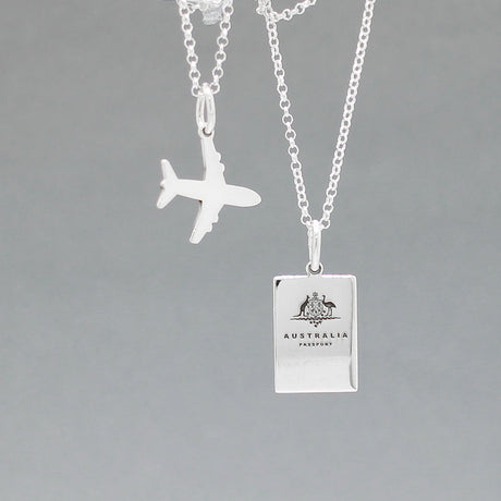 Our Australian Passport Mini Replica Silver Pendant captures all the intricate details of a passport cover. Meticulously crafted from sterling silver, it boasts a dazzling high-polished finish.  Dimensions: Passport: 10mm wide by 14mm high Airplane: 14mm wide by 14mm high Bail: Fits up to a 2.5mm chain for versatile wear. Chain: Includes a 1.4mm sterling silver belcher Rolo chain, available in various lengths to suit your style preference.