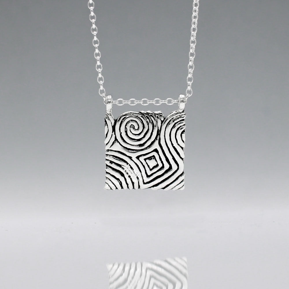 Inspired by the Newgrange Stone Dimensions: 20mm wide x 24mm high (including bail), 2mm thick Finish: Oxidized to accentuate the design, with a high polished finish Material: Handmade with 0.50 sterling silver Chain: 1.7mm sterling silver rolo chain included (select chain size below) Celebrate the ancient beauty of Newgrange with our Cropped Square Silver Pendant. This unique piece is expertly crafted to honor Ireland's rich heritage.