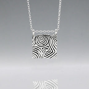 Inspired by the Newgrange Stone Dimensions: 20mm wide x 24mm high (including bail), 2mm thick Finish: Oxidized to accentuate the design, with a high polished finish Material: Handmade with 0.50 sterling silver Chain: 1.7mm sterling silver rolo chain included (select chain size below) Celebrate the ancient beauty of Newgrange with our Cropped Square Silver Pendant. This unique piece is expertly crafted to honor Ireland's rich heritage.