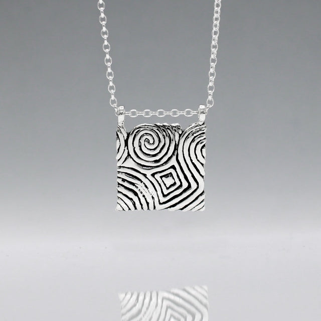Inspired by the Newgrange Stone Dimensions: 20mm wide x 24mm high (including bail), 2mm thick Finish: Oxidized to accentuate the design, with a high polished finish Material: Handmade with 0.50 sterling silver Chain: 1.7mm sterling silver rolo chain included (select chain size below) Celebrate the ancient beauty of Newgrange with our Cropped Square Silver Pendant. This unique piece is expertly crafted to honor Ireland's rich heritage.