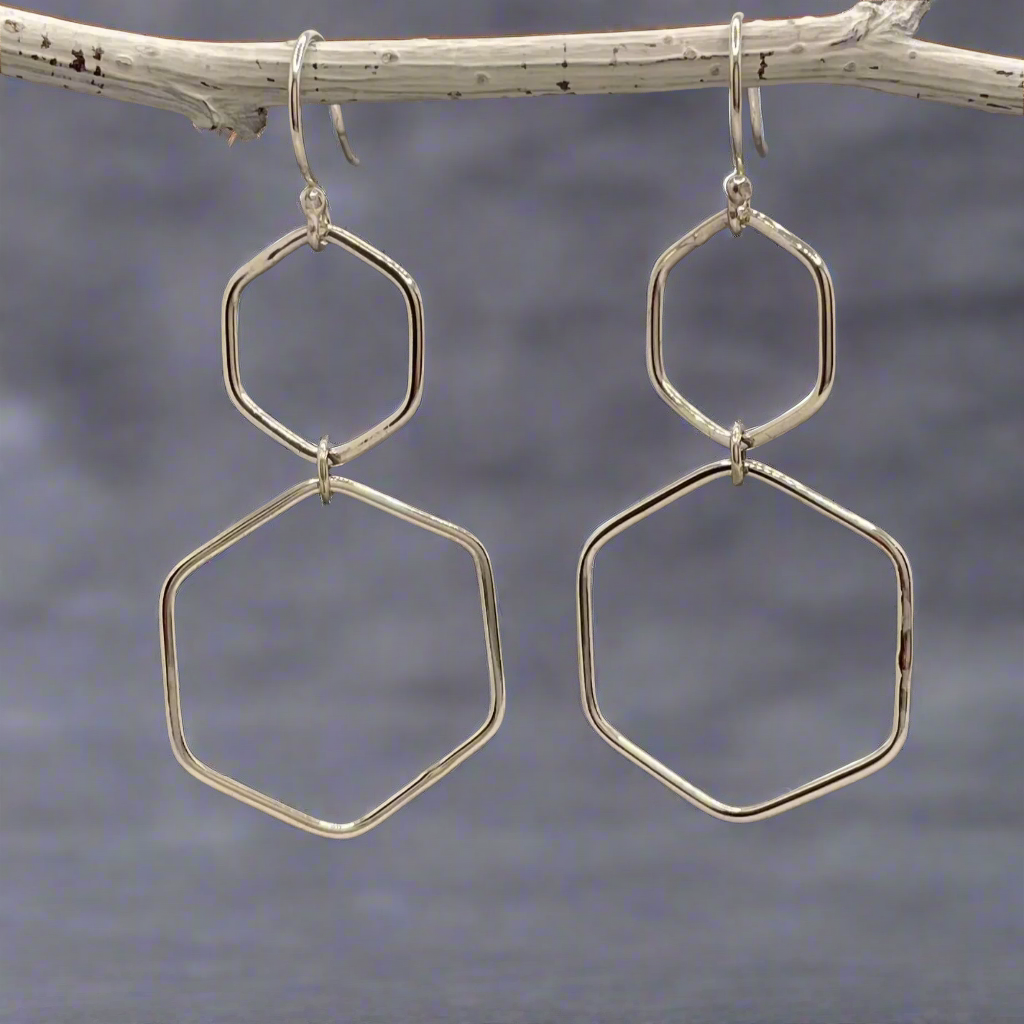 Celebrate geometric elegance with the Saha Double Hexagon Silver Hoop Earrings. These handcrafted sterling silver earrings feature a smaller hexagon measuring 18 mm in diameter, paired with a larger 29 mm hexagon for a striking, layered look. Inspired by honeycomb patterns, their whimsical design is perfect for adding a unique touch to any outfit. Ireland jewellery