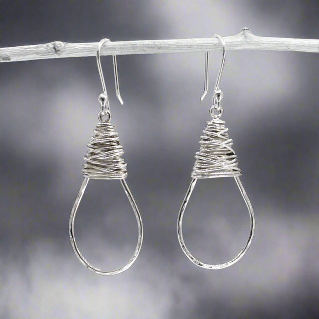 The Saha Drop Shape with Wire Wrap Silver Earrings bring timeless elegance to your jewellery collection. Handcrafted from sterling silver, these earrings feature a graceful drop shape accentuated with intricate wire wrapping. The highly polished finish adds a refined touch, making them ideal for both everyday wear and special occasions. Ireland jewellery