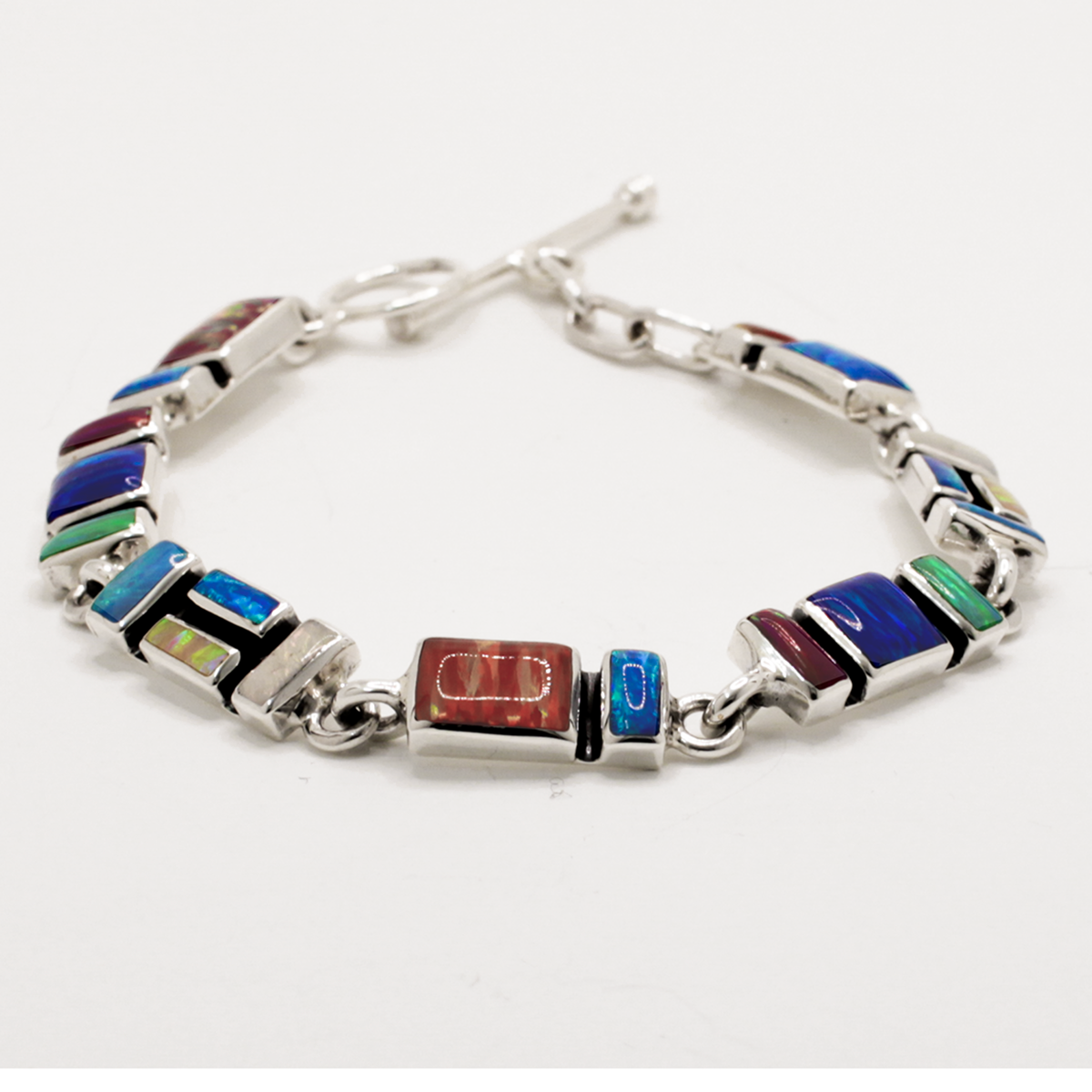 Add a vibrant pop of colour to your style with the Sleveen bracelet. Seven colorful rectangle opalescent pieces display a mesmerizing mosaic, measuring 7mm in width and 3mm deep. This bracelet is finished with a toggle clasp and measures 19cm in length, crafted in .925 silver and featuring colored resins inspired by the beautiful houses of Kinsa