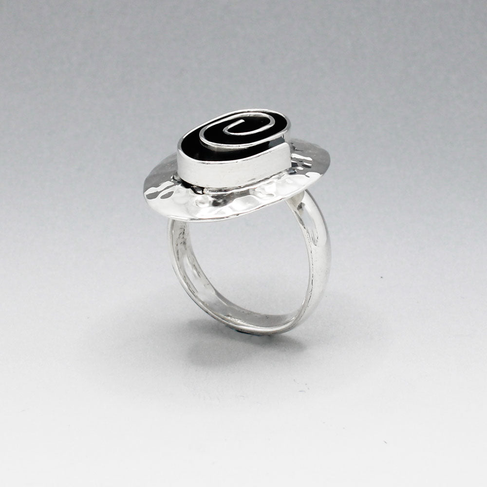 Tara - Oxidised Spiral On Hammered Oval Silver Ring  Discover the unique charm of our Tara ring, featuring an exquisite oxidised spiral design set on a hammered oval silver base. This striking piece measures 20mm wide by 25mm long, with the spiral itself measuring 12mm wide by 17mm long.  The adjustable band ensures a perfect fit, ranging from size 7 (European size 54) to size 9 (European size 59). Crafted from solid sterling silver, the 4mm wide band offers durability.