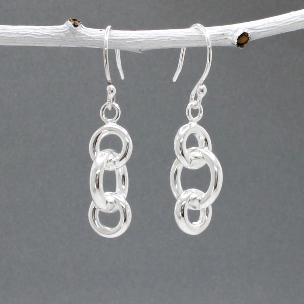 These handmade dangle earrings feature three interlocked rings in two different diameters, crafted from sterling silver with a highly polished finish.  Features:  Interlocked Design: Three rings in two different diameters for a unique look Large ring diameter: 12mm Small ring diameter: 9mm Ring Thickness: 2.5mm Total Length: 22mm Overall Length: 40mm from the top of the ear wire Material: Sterling silver Finish: Highly polished for a brilliant shine