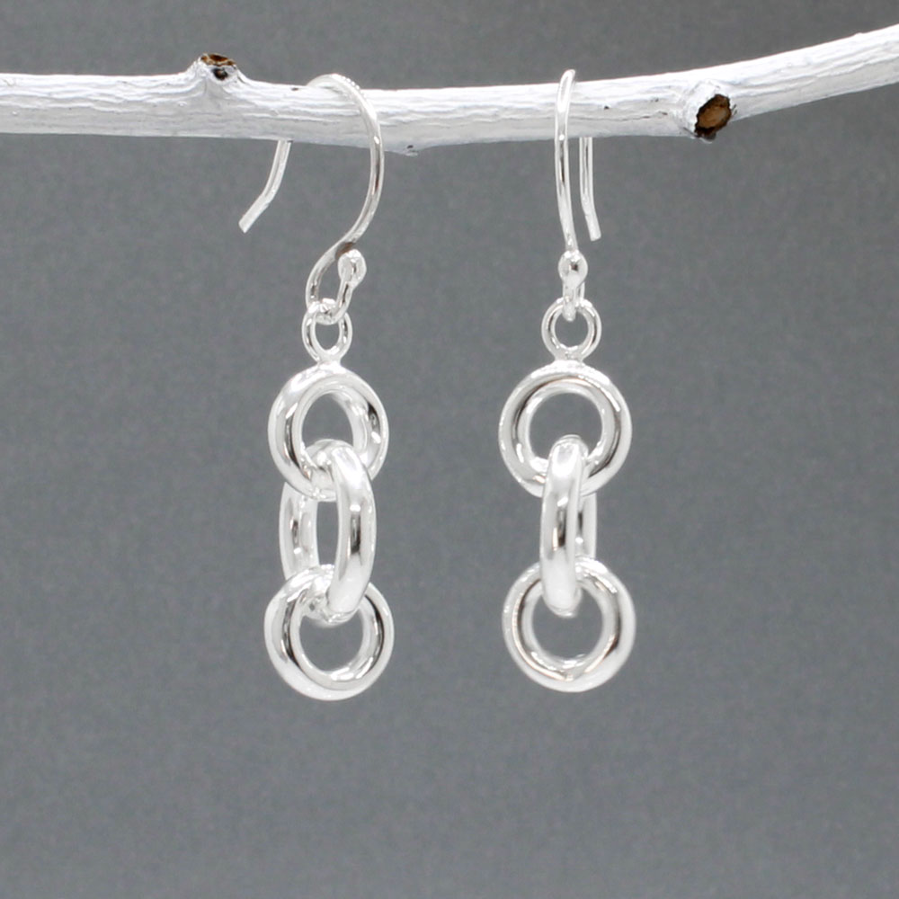 These handmade dangle earrings feature three interlocked rings in two different diameters, crafted from sterling silver with a highly polished finish.  Features:  Interlocked Design: Three rings in two different diameters for a unique look Large ring diameter: 12mm Small ring diameter: 9mm Ring Thickness: 2.5mm Total Length: 22mm Overall Length: 40mm from the top of the ear wire Material: Sterling silver Finish: Highly polished for a brilliant shine