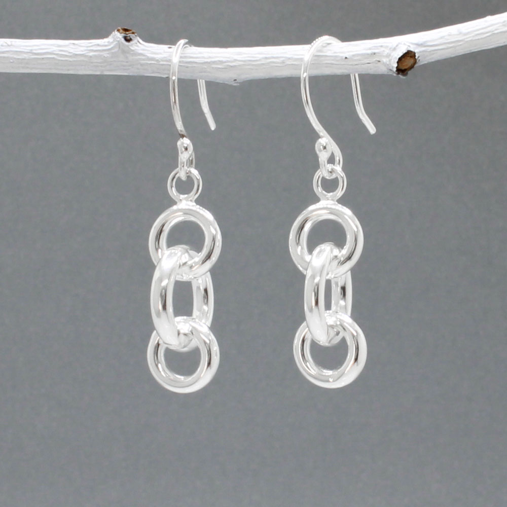 These handmade dangle earrings feature three interlocked rings in two different diameters, crafted from sterling silver with a highly polished finish.  Features:  Interlocked Design: Three rings in two different diameters for a unique look Large ring diameter: 12mm Small ring diameter: 9mm Ring Thickness: 2.5mm Total Length: 22mm Overall Length: 40mm from the top of the ear wire Material: Sterling silver Finish: Highly polished for a brilliant shine