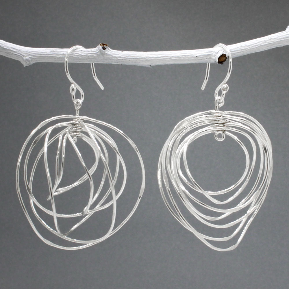 Tara - Twisting Multi-Circle Silver Earrings - Dangle  Design: Seven graduated hoops interconnected, creating an organic circle shape  Movement: Rotates when worn, adding whimsical and dynamic movement Features: Lightweight, highly polished silver Fastening: Sterling silver French wire Measurements: Width: 37 MM at its widest point Length: 55 MM from the top of the French wire. Jewellery in Ireland.