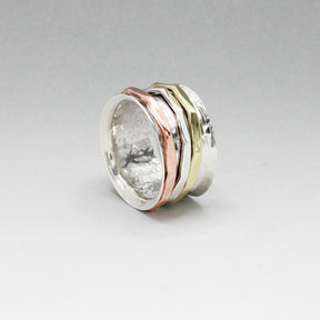 The Tara Mixed Metal Spinning Silver Ring is a true statement piece, boasting a 13mm-wide band for a bold yet comfortable fit. Its intricate design features three inner bands crafted from brass, copper, and silver, each measuring 2mm wide. This ring is a stunning fusion of style and craftsmanship, sure to turn heads wherever you go.