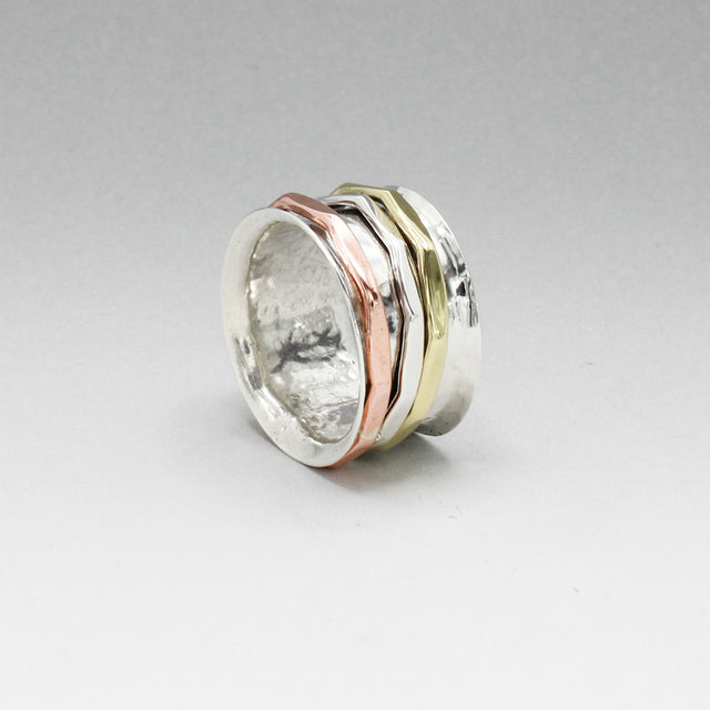 The Tara Mixed Metal Spinning Silver Ring is a true statement piece, boasting a 13mm-wide band for a bold yet comfortable fit. Its intricate design features three inner bands crafted from brass, copper, and silver, each measuring 2mm wide. This ring is a stunning fusion of style and craftsmanship, sure to turn heads wherever you go.