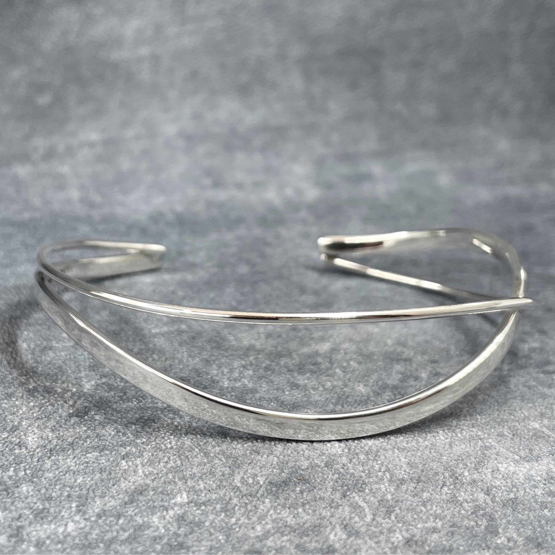 Uisce - Double Wave Cuff Silver Bracelet, meticulously handcrafted with sterling silver and boasting a striking high-polished finish. Each cuff features a captivating Double Wave design, accentuated by polished silver. This handmade piece offers a thickness of 1.5 millimeters and can be gently adjusted for a perfect fit.</p> <p>Measuring 14.5 cm on the inner length and 15.5 cm on the outer length from end to end, with a width of 1.2 cm at its widest point and a 3 cm gap. Ireland.
